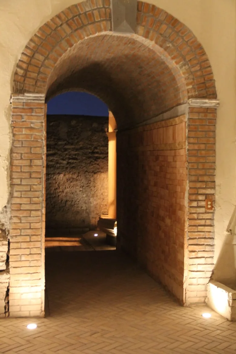 Arco de ladrillo de medio punto que abre a un patio de piedra.