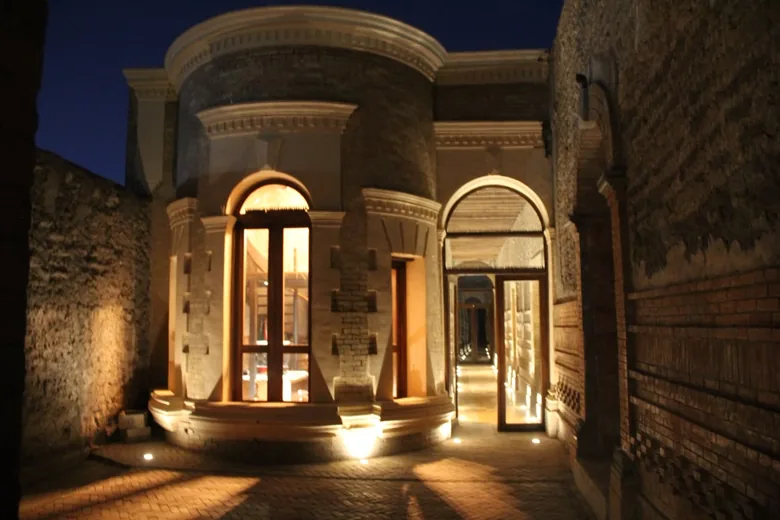 El patio interior de noche, con el cuerpo curvo de sillería iluminado desde el piso.