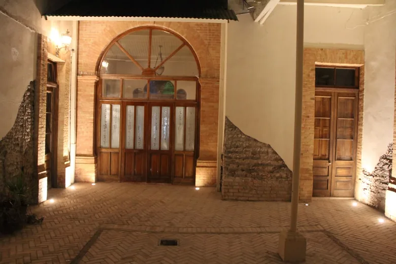 El patio interior de noche, con piso de ladrillo en espiga y grandes puertas de arco con vidriería.