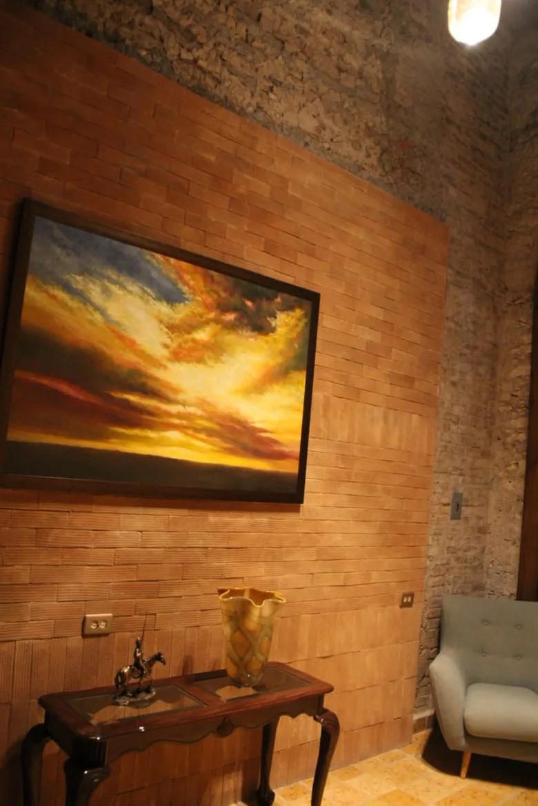 Sala de espera con un óleo de un cielo al atardecer sobre muro de ladrillo labrado.