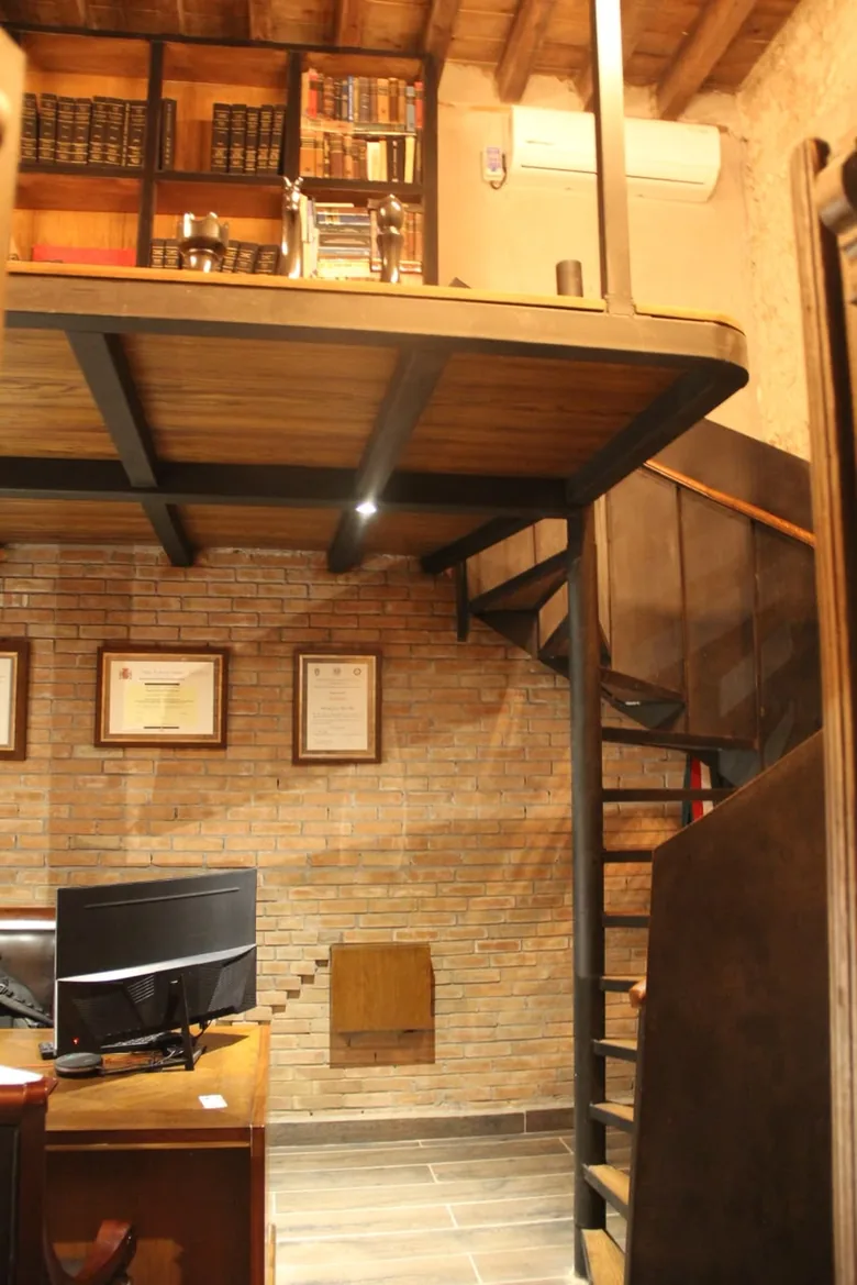 Oficina de muro de ladrillo con tapanco de madera y escalera de caracol de herrería.